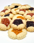 A pile of True Delicious Biscotti Fruit Blossoms Cookies - Assorted Flavors, made with natural ingredients and filled with orange, red, and dark purple fruit jams, displayed on a white background.