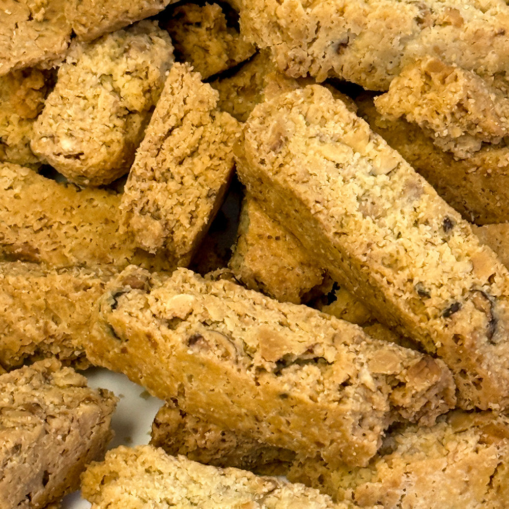 A close-up of True Delicious 2lbs Sugar Free Almond Biscotti Bits shows golden-brown, crunchy pieces made with almond flour. These keto-friendly treats feature visible nut bits and are stacked together.