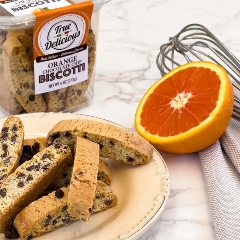 Orange chocolate chip biscotti on a plate with a half-cut orange and packaging in the background.