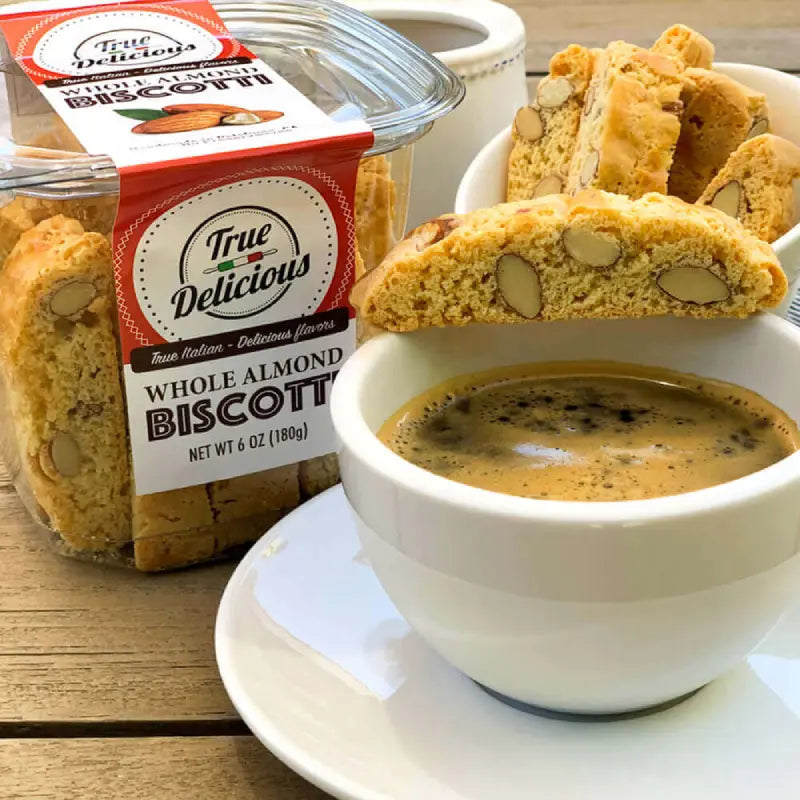Jar of True Delicious Whole Almond Biscotti with a cup of coffee on a wooden surface
