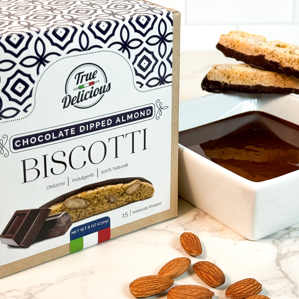 An Elegant Box of True Delicious Chocolate Dipped Almond Biscotti, individually wrapped, rests on a marble counter with almonds and chocolate—a perfect gourmet gift for authentic Italian biscotti lovers.