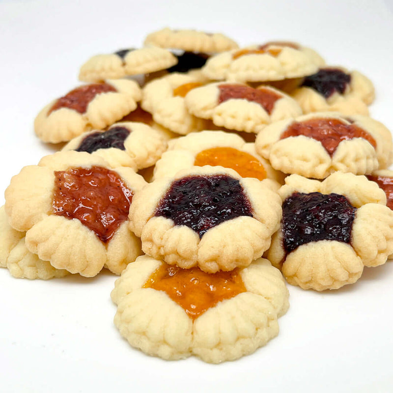 A pile of True Delicious Biscotti Fruit Blossoms Cookies - Assorted Flavors, made with natural ingredients and filled with orange, red, and dark purple fruit jams, displayed on a white background.