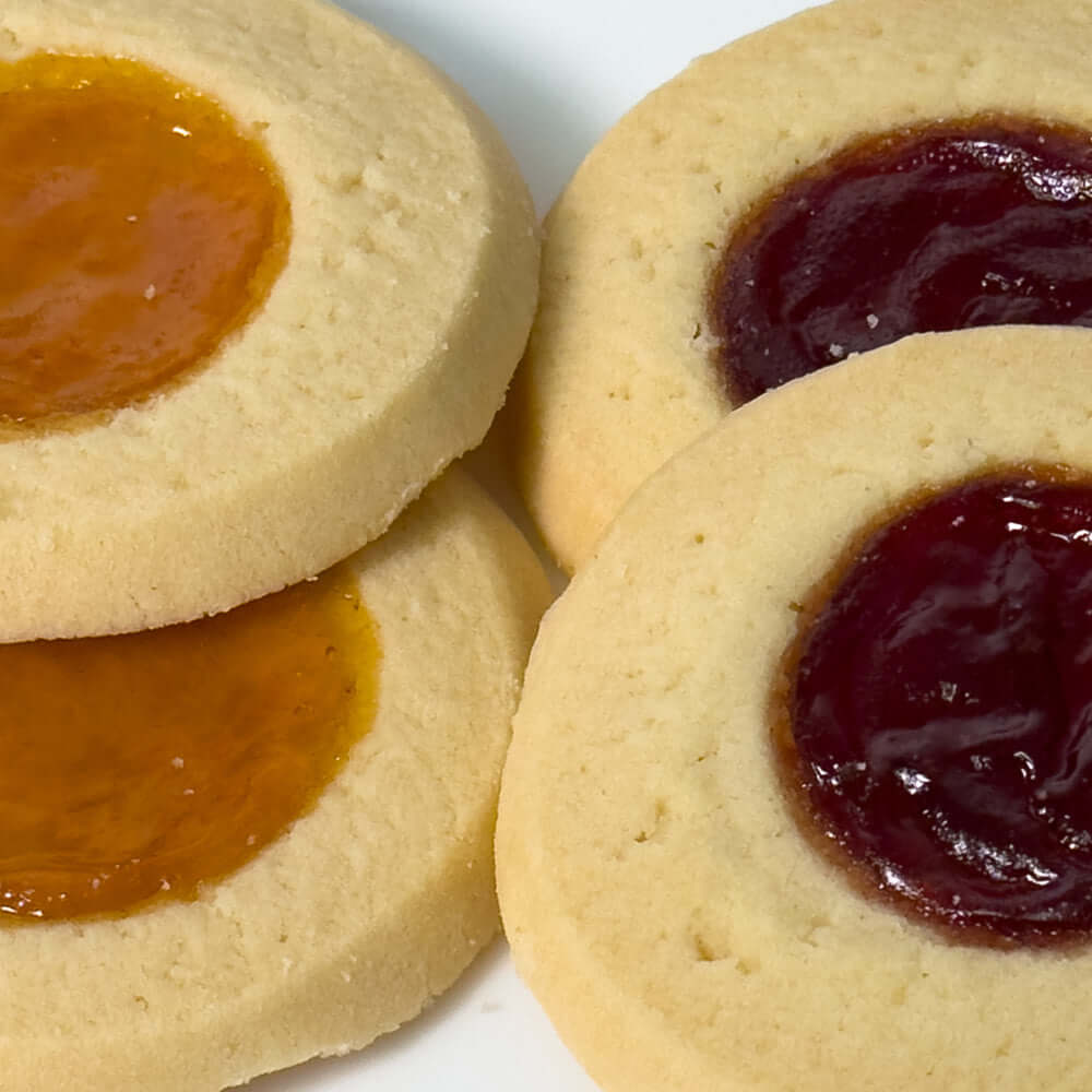 Close-up of True Delicious Jam Cookies Apricot Raspberry—four buttery shortbread cookies with apricot and raspberry jam centers, arranged on a white surface. Classic treats perfect for satisfying any sweet craving.