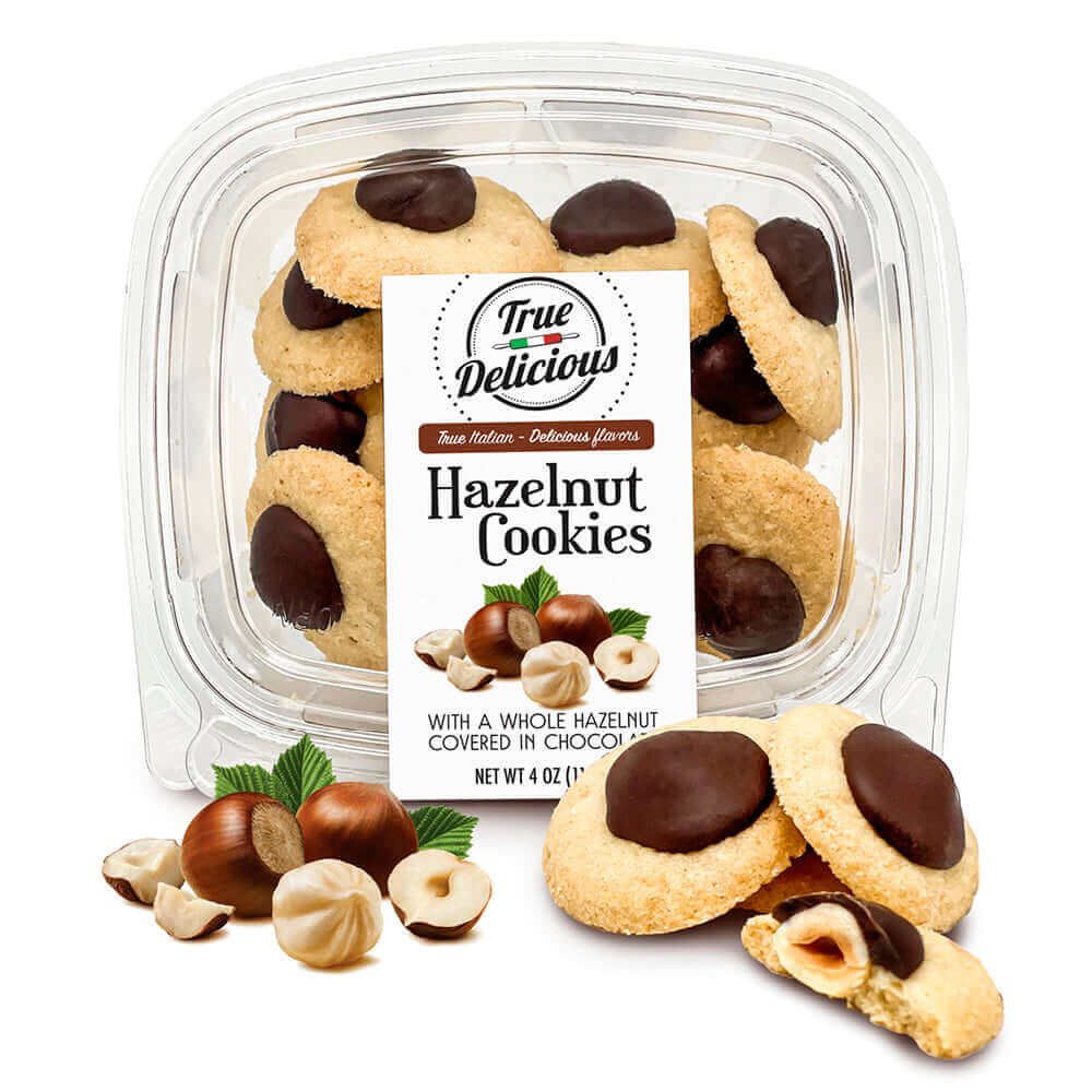 A clear plastic container of True Delicious Hazelnut Cookies with Dark Chocolate, made with Non-GMO ingredients, featuring round cookies topped with whole hazelnuts and dipped in chocolate, plus a product label and hazelnut images on the front.